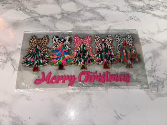 Decorative Christmas tree figurines with colorful patterns on a clear plastic card with 'Merry Christmas' text, placed on a marble surface.